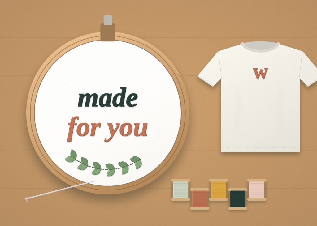 Embroidery studio flat lay with a hoop, thread spools and a stitched tee